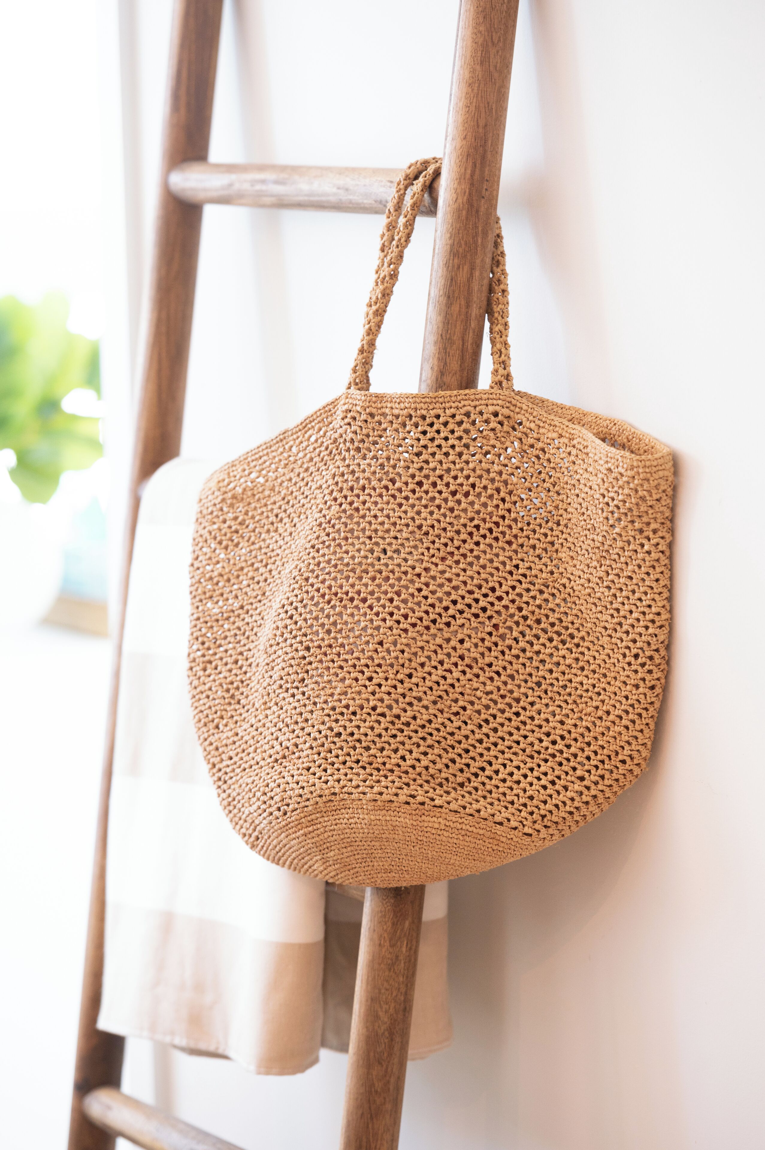 A woven bag hanging on a wooden ladder against a white wall.