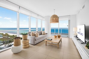 A modern living room with a large window overlooking the sea, a sofa with cushions, a coffee table, and a television. - Monte Carlo by Miami Vacations (Miami Beach)