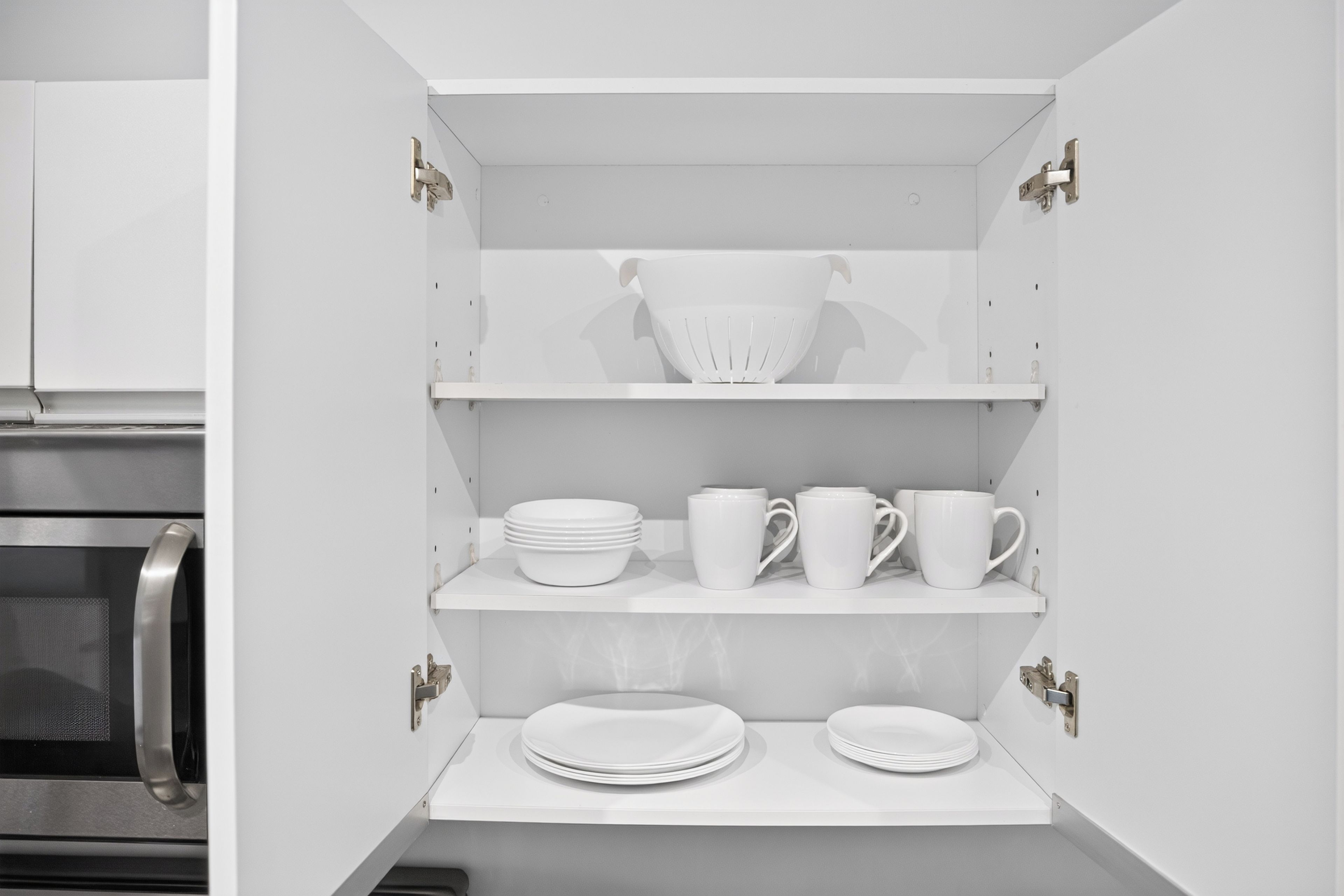 A white kitchen cabinet with shelves holding plates, bowls, and cups.