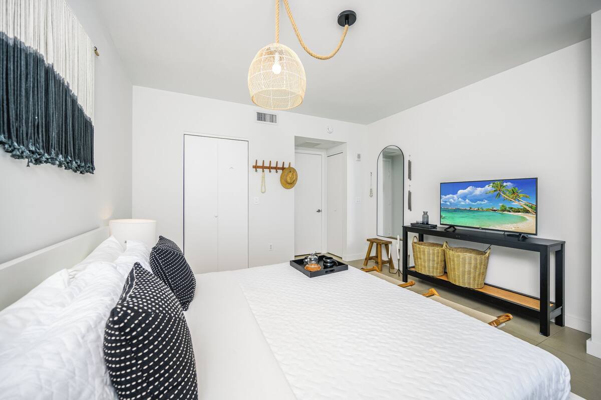 A modern bedroom with a large bed, a TV, and a hanging light fixture.
