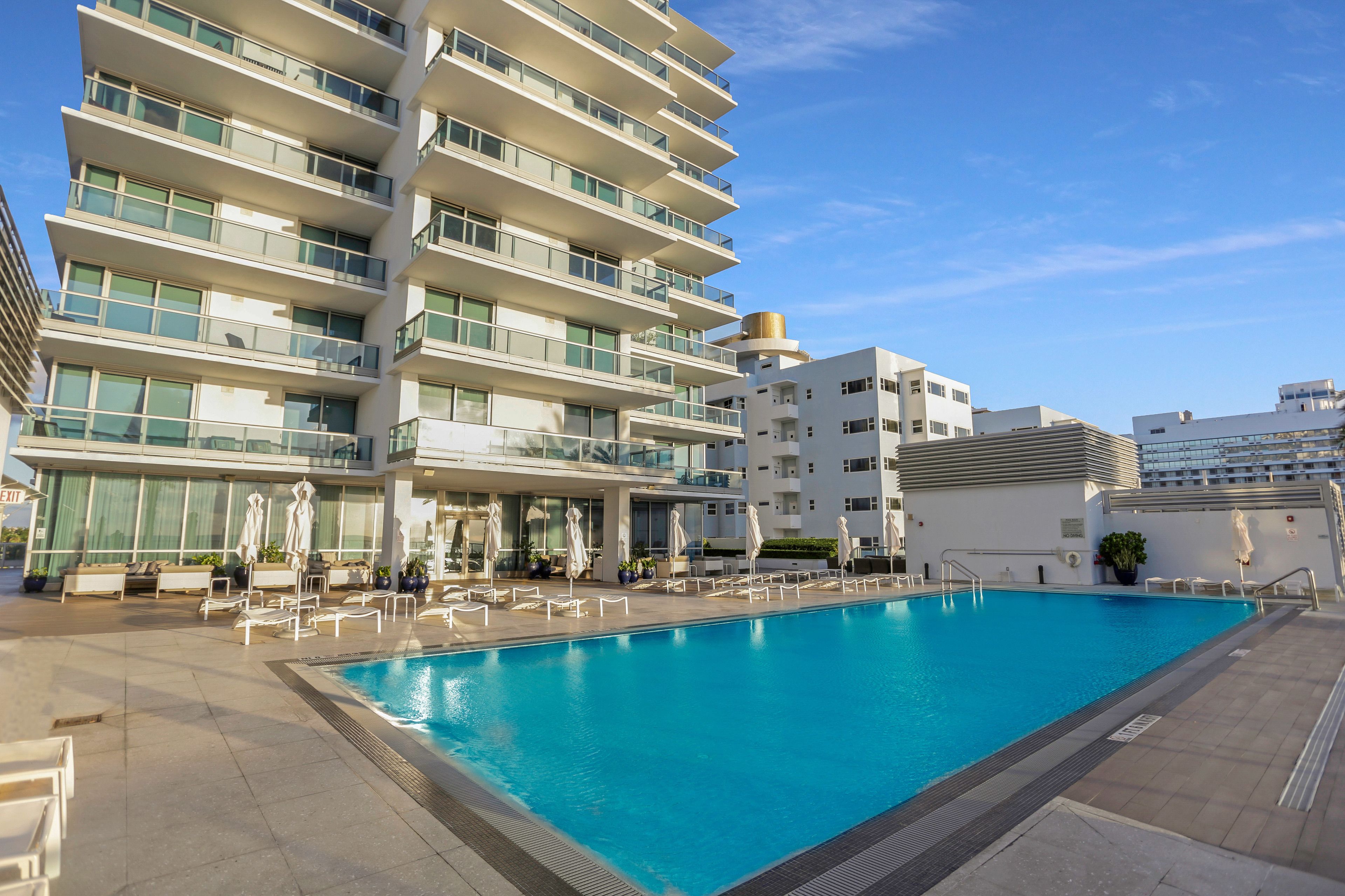 A modern hotel with a swimming pool, multiple balconies, and outdoor seating areas.