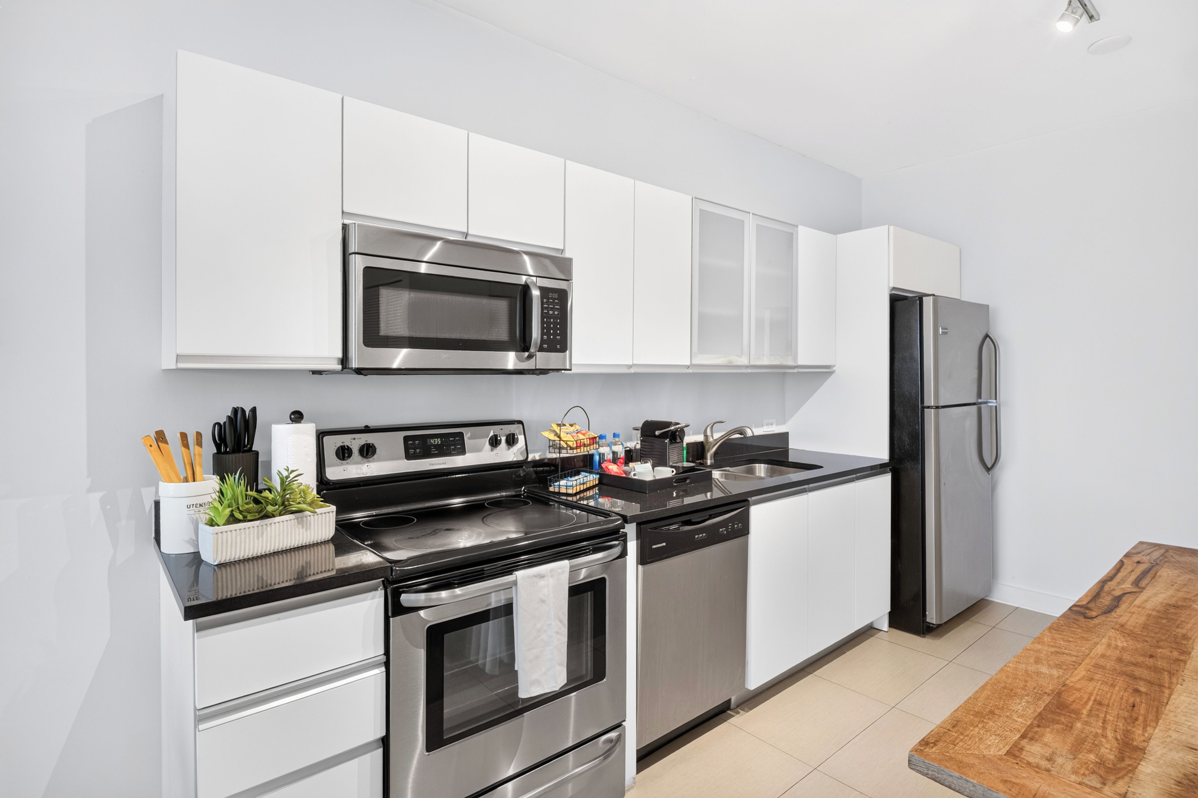 A modern kitchen with stainless steel appliances, white cabinetry, and a wooden dining table.