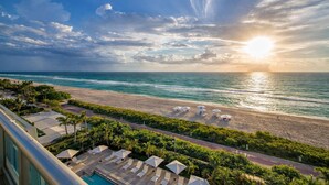 A beach view with a poolside area, lounge chairs, and umbrellas. - Monte Carlo by Miami Vacations (Miami Beach)