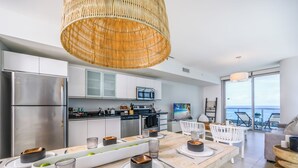 A modern kitchen with stainless steel appliances, a dining area with a long table, and a view of the sea through large windows. - Monte Carlo by Miami Vacations (Miami Beach)
