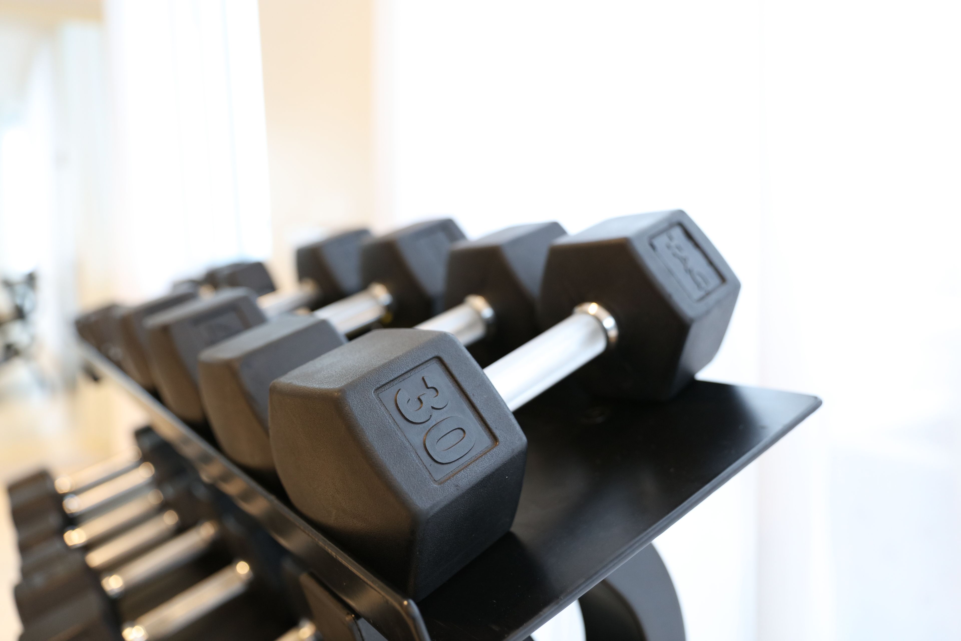 A row of black dumbbells with weight markings on a black rack.