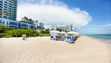 Na praia, areia branca, espreguiçadeiras, guarda-sóis