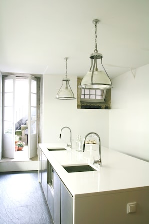 A kitchen with a double sink, pendant lights, and a view of a balcony with potted plants. - Rosa Et Al Townhouse (Porto)