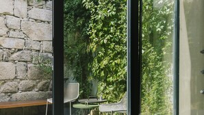 A modern room with a glass wall, a bench with cushions, a small table, and a chair. - Rosa Et Al Townhouse (Porto)