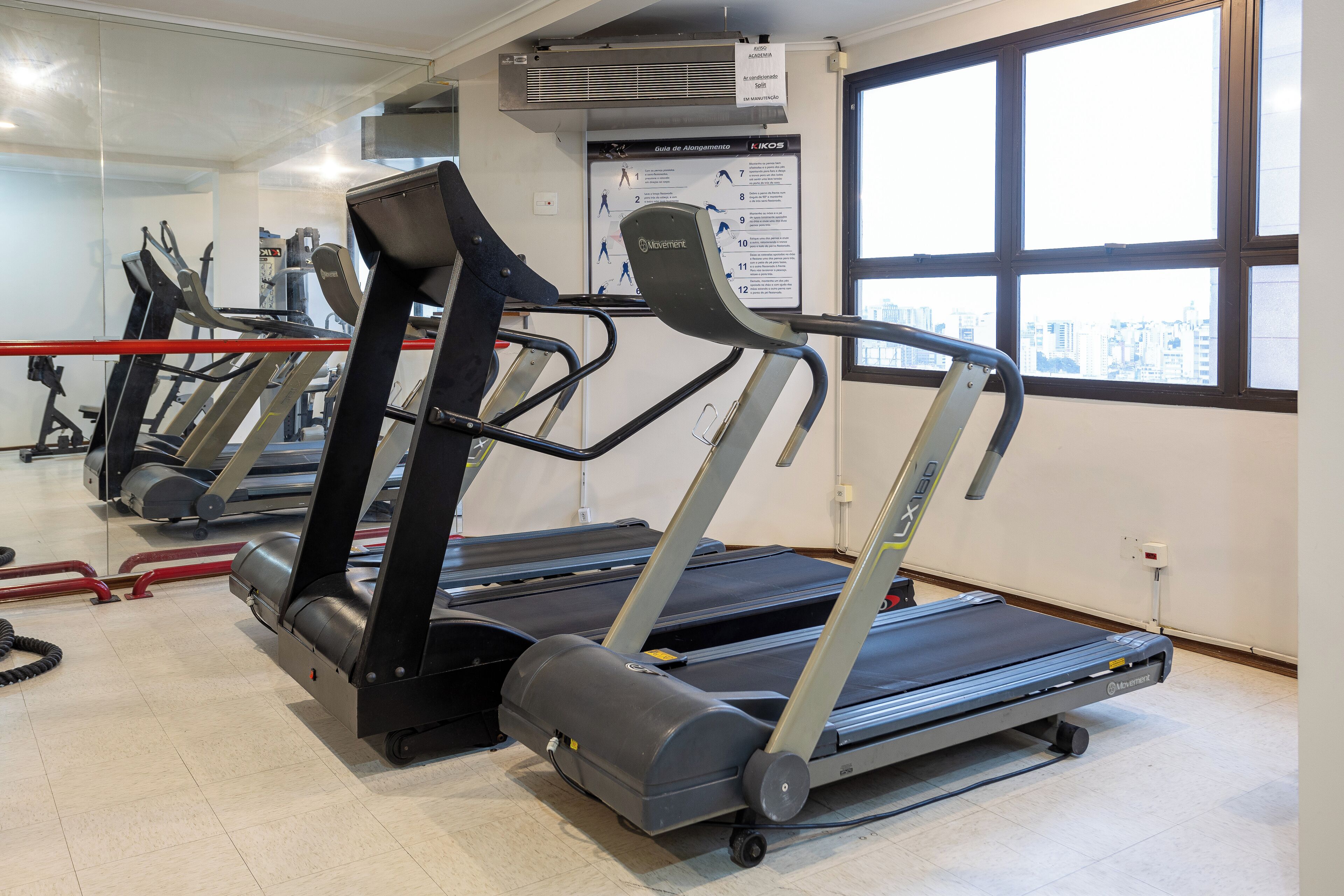 Un gimnasio con cintas de correr, bicicletas estáticas y un espejo grande.