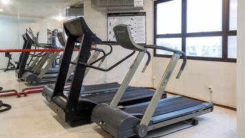 Un gimnasio con cintas de correr, bicicletas estáticas y un espejo grande.
