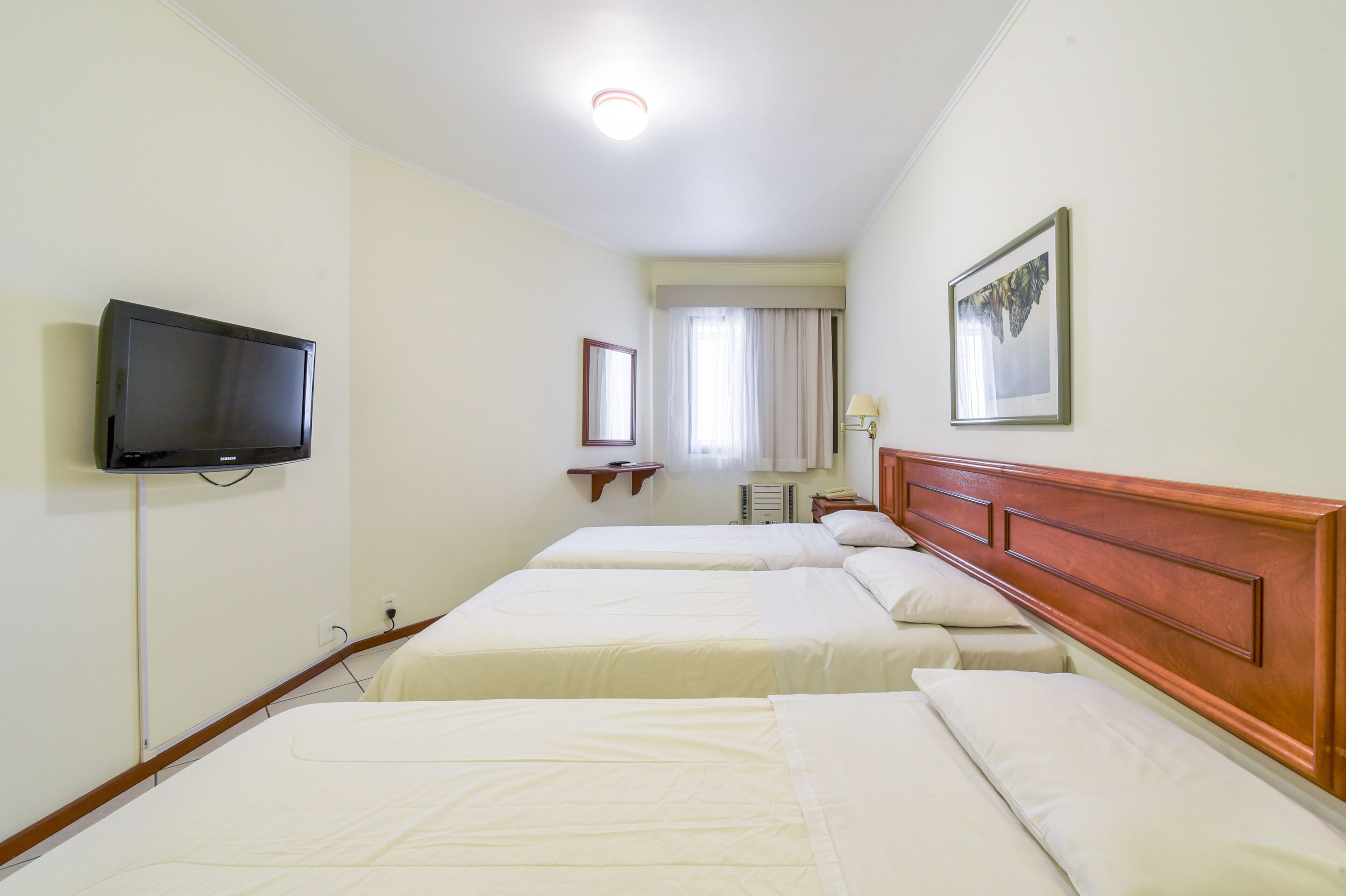 Habitación de hotel con dos camas, televisión, ventana con cortinas y un cuadro en la pared.