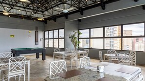 A spacious indoor area with a pool table, multiple dining tables, and chairs. Large windows provide views of the cityscape. - Park Tower Campinas Residence by Nacional Inn (Campinas)