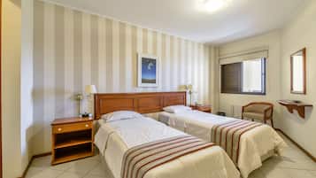 Habitación de hotel con dos camas, una mesita de noche de madera, una silla, una ventana con persianas y un cuadro enmarcado en la pared.