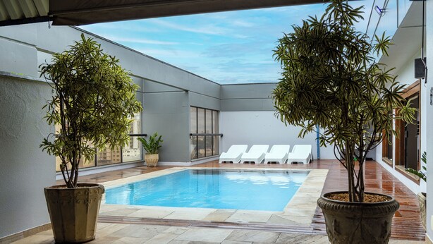 A swimming pool with two potted plants, white lounge chairs, and a tiled deck. - Park Tower Campinas Residence by Nacional Inn (Campinas)