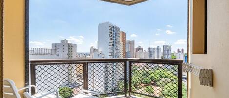 Un balcón con vistas a un paisaje urbano, que incluye edificios altos y una zona verde con parque.