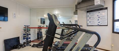 A gym with treadmills, weight machines, and a mirrored wall.