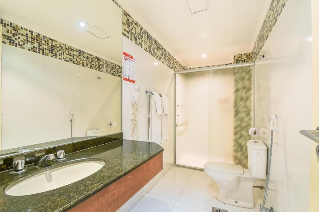 A modern bathroom with a granite countertop sink, a white toilet, and a glass-enclosed shower.