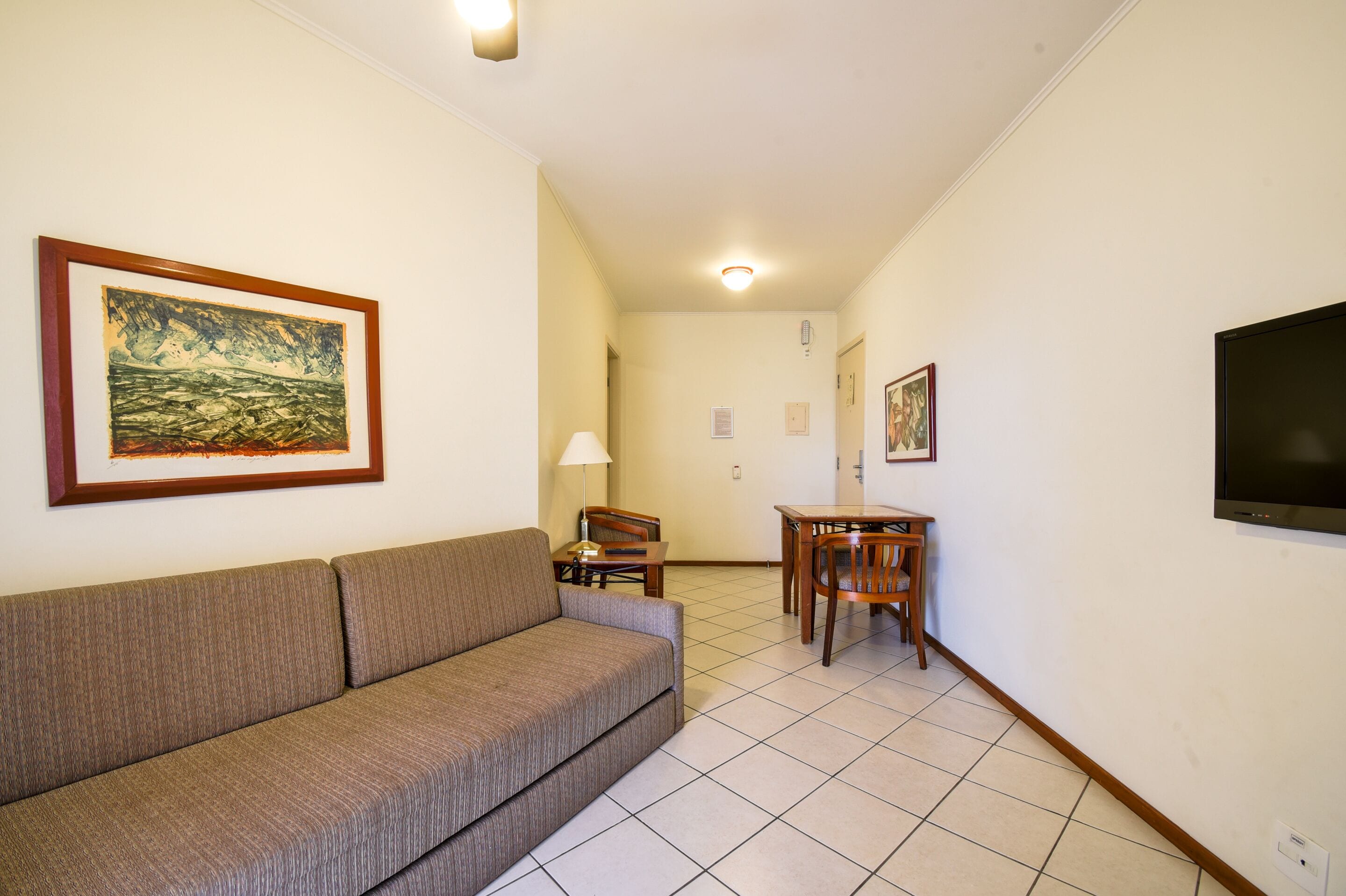 A living room with a sofa, a dining table with chairs, a TV mounted on the wall, and a framed painting.