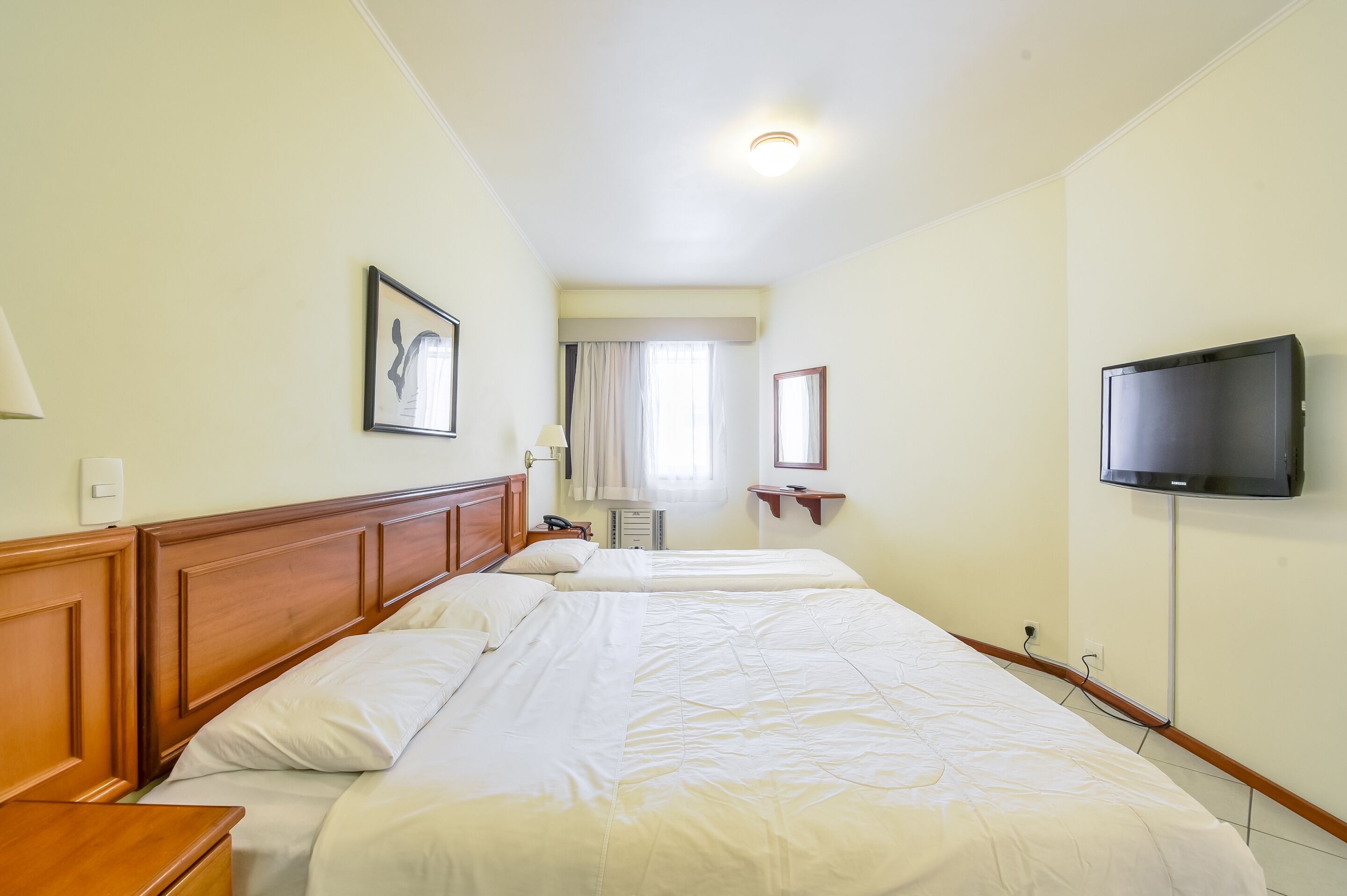 Een hotelkamer met een groot bed, nachtkastjes, een televisie en een raam met gordijnen.