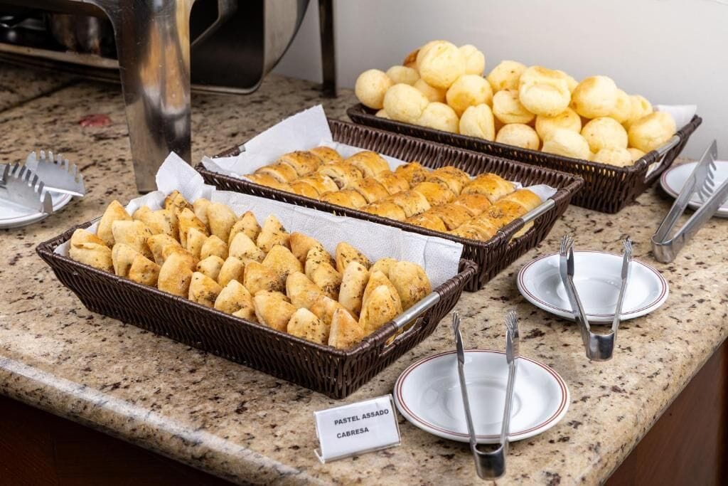 A buffet table with various food items, including bread rolls and pastries, with serving utensils and plates.
