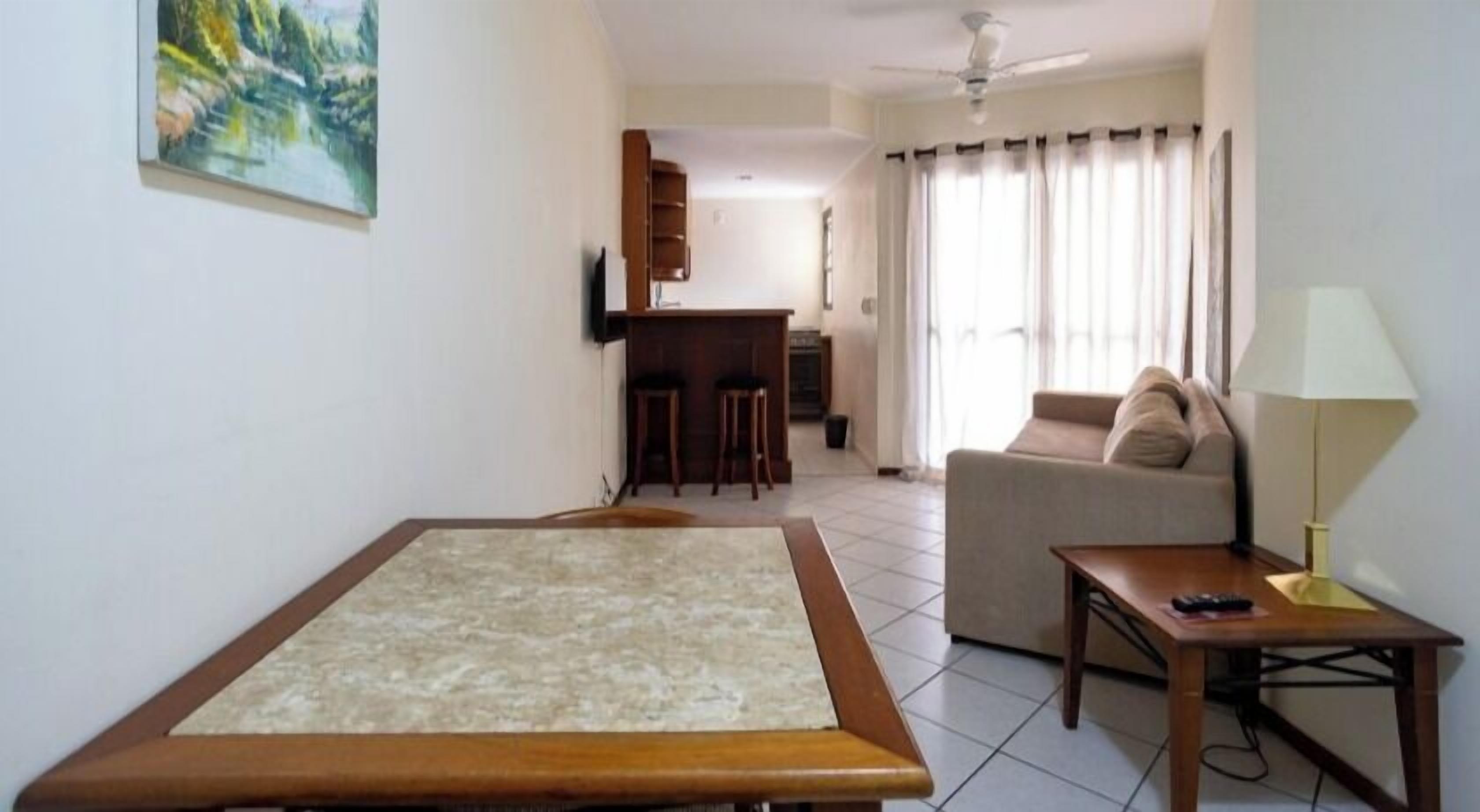Una habitación con cama, sofá, una mesita, lámpara, televisor, zona de cocina y un cuadro en la pared.