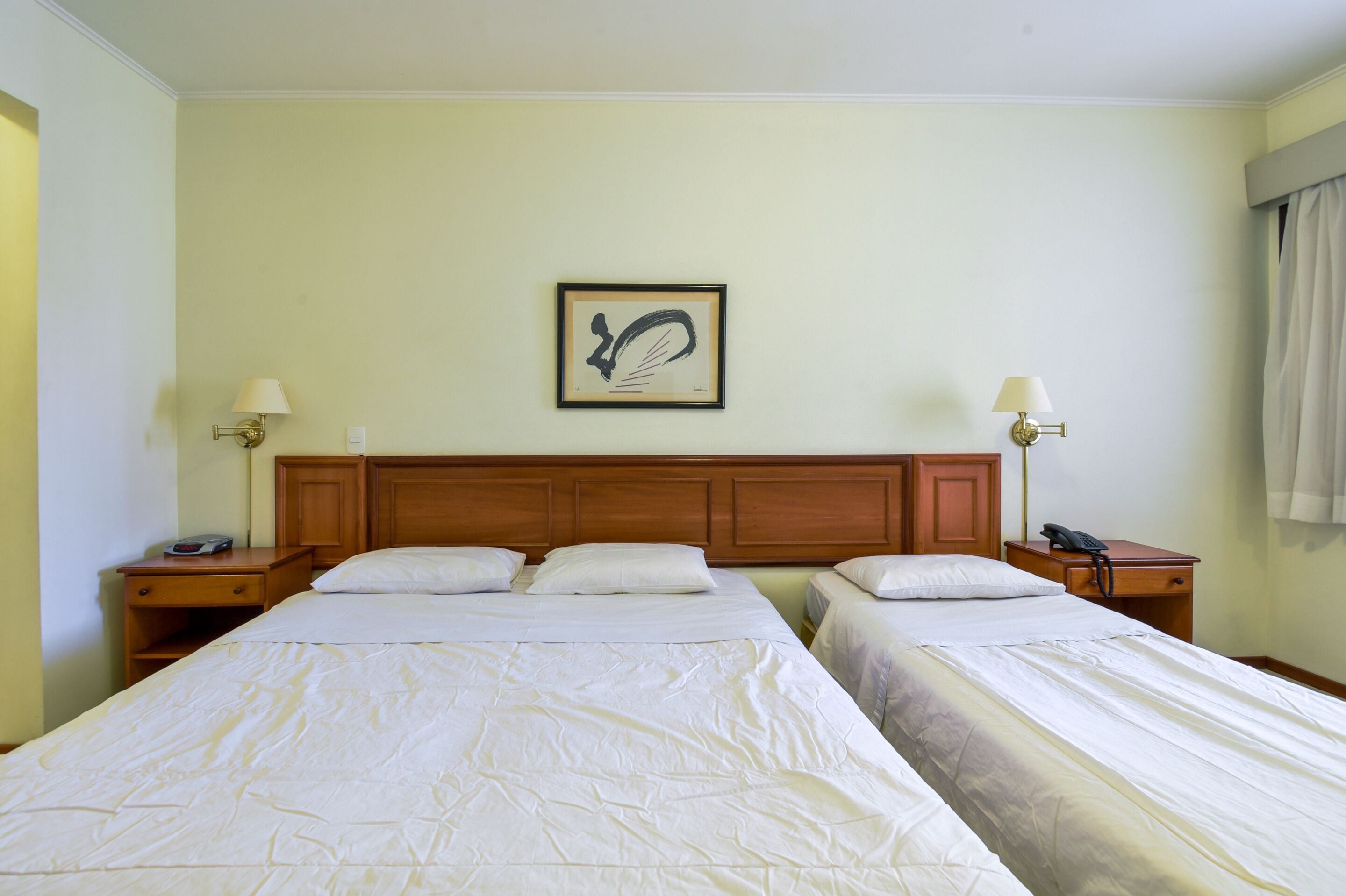 Een hotelkamer met twee eenpersoonsbedden, een houten hoofdbord, nachtkastjes met lampen en een kunstwerk in een lijst aan de muur.