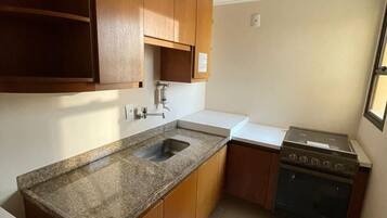 A compact kitchen with wooden cabinets, a granite countertop, a built-in stove, and a sink.