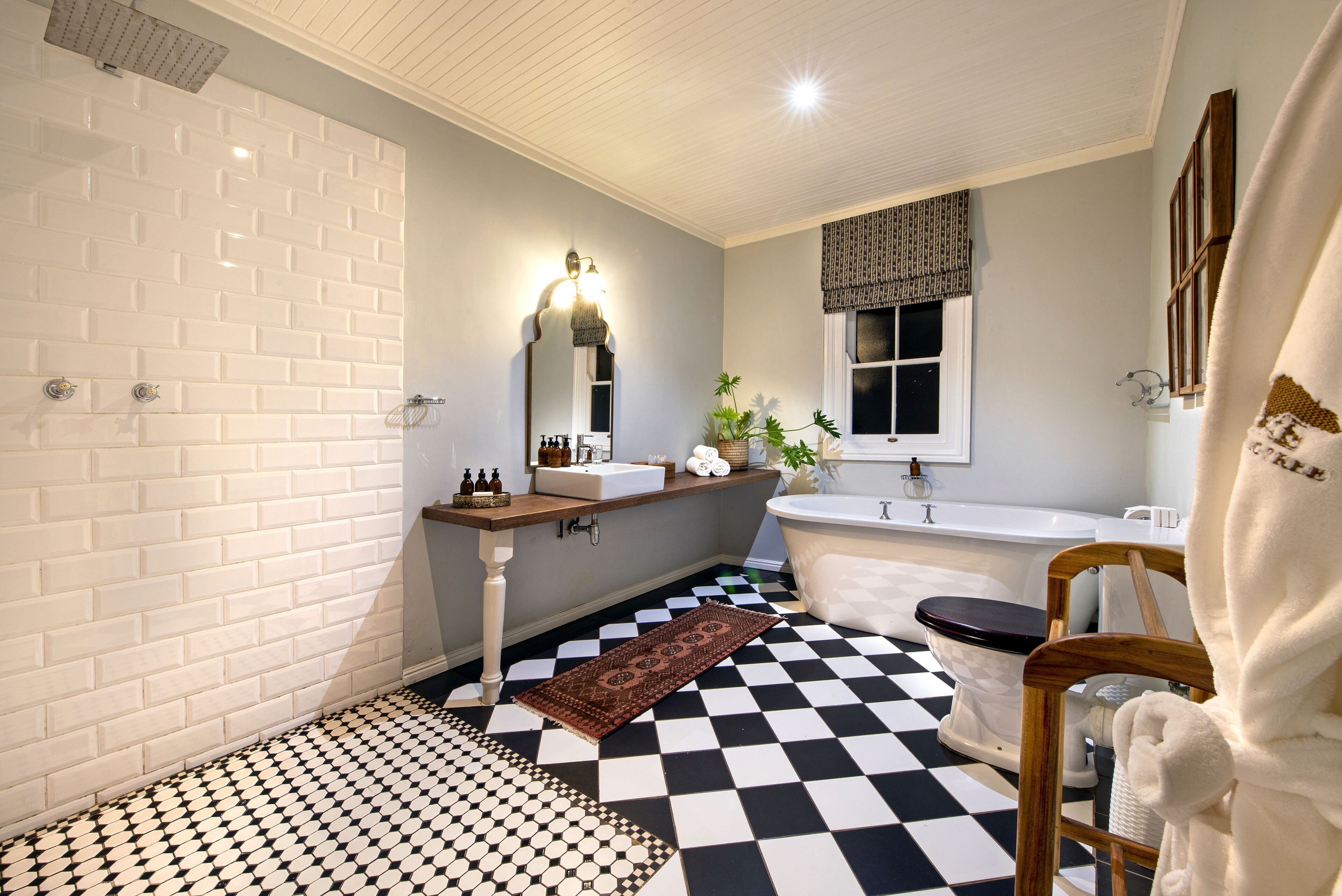 A bathroom with a checkered floor, a white bathtub, a wooden vanity, and a mirror with lights.