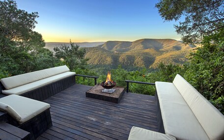 A deck with a fire pit and outdoor seating, overlooking a mountainous landscape.