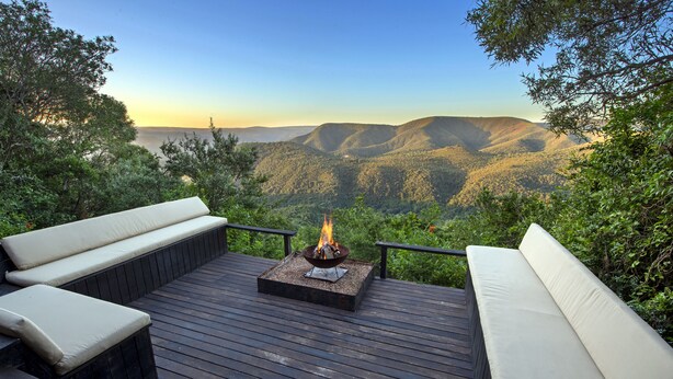 Une terrasse dotée d’un foyer extérieur et de sièges, offrant une vue sur un paysage montagneux.