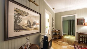 Une pièce décorée d’un tableau encadré, d’un radiateur de style ancien, d’une chaise en osier et d’un tapis à motifs.