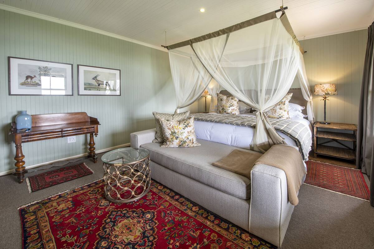 A bedroom with a four-poster bed, a sofa, a small table, and a lamp.