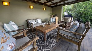 Un patio couvert, aménagé avec du mobilier en bois, comprenant un canapé et des fauteuils, une table en bois et deux lampes fixées au mur.