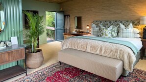 Une chambre à coucher comprenant un lit, un banc, une table de chevet, un miroir, une plante en pot et une vue sur l’extérieur.