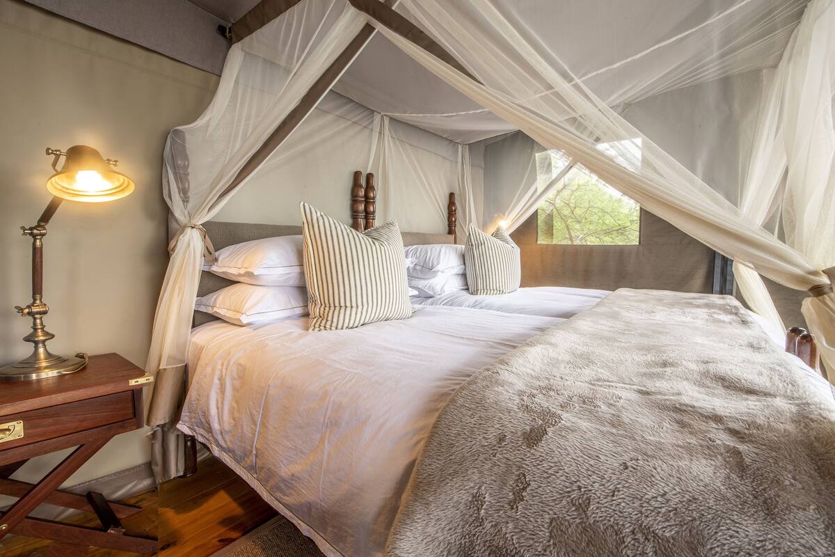 A bedroom with a canopy bed, a bedside lamp, and a wooden nightstand.