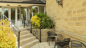 A patio area with outdoor seating, a stone wall, and a staircase leading to an entrance. - The Gibside Hotel (Newcastle-upon-Tyne)