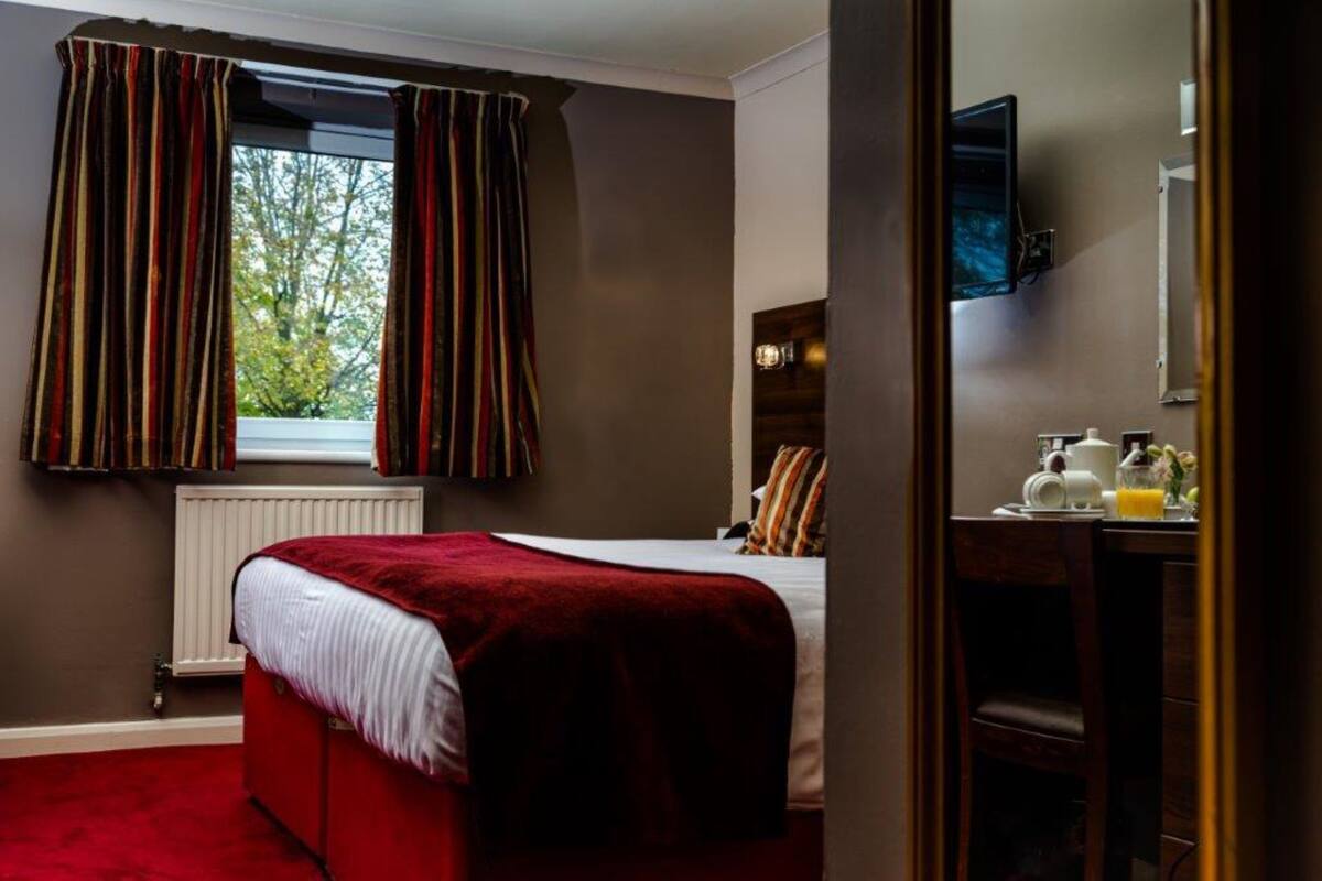 A hotel room with a bed, a window with curtains, a radiator, a television, and a breakfast tray on a table.