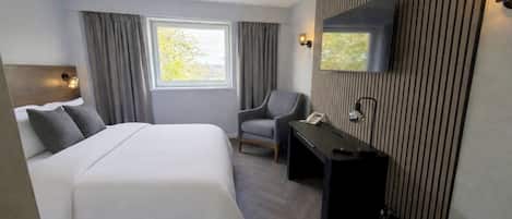 Habitación de hotel con cama, escritorio, silla, televisor montado en la pared y ventana con cortinas.