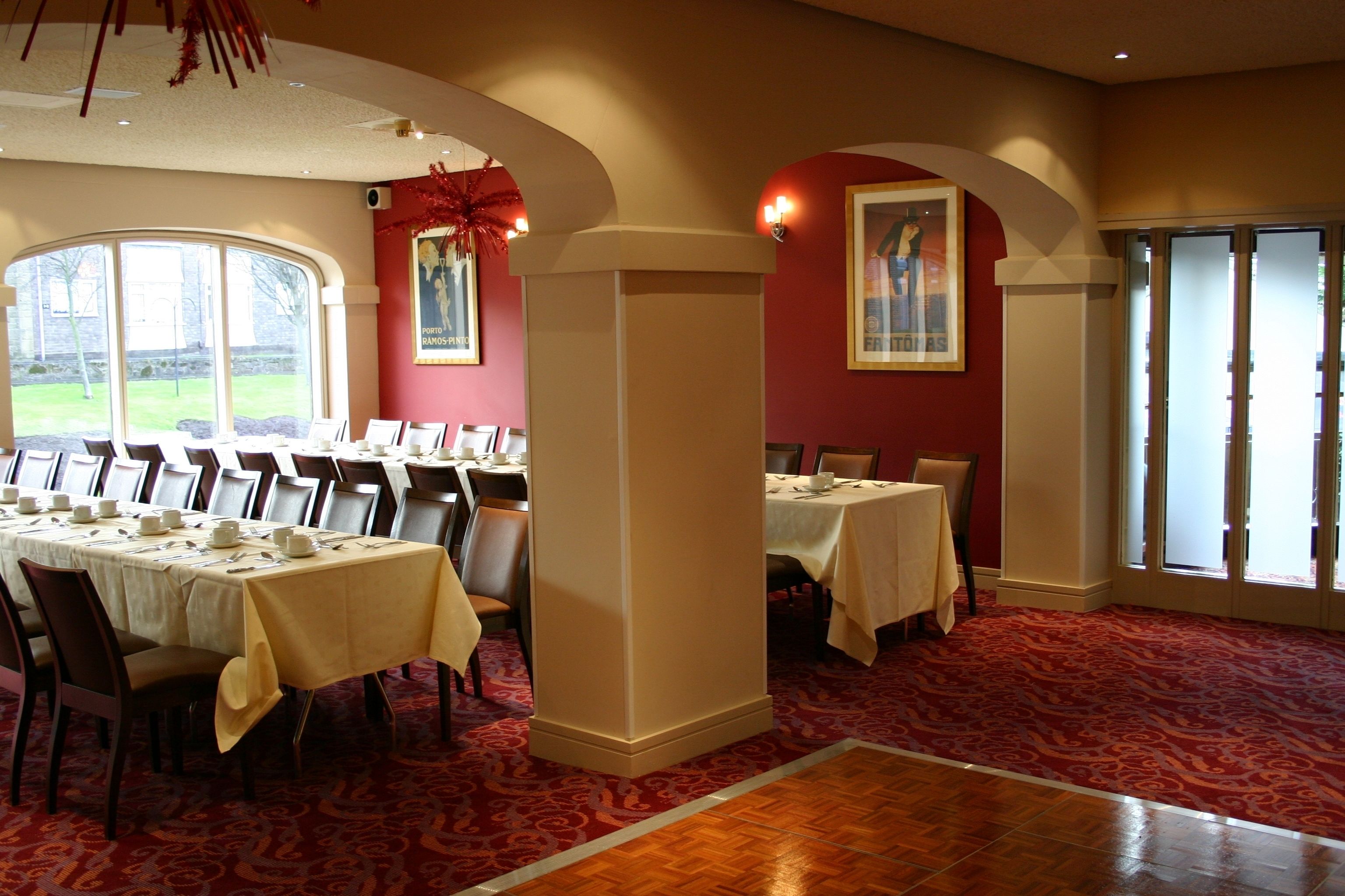Un espace repas avec des tables dressées pour le repas, une grande fenêtre et un sol recouvert d’un tapis rouge.