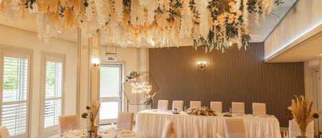 Un salón de banquetes con mesas redondas dispuestas para cenar, un techo decorativo y una pared con líneas verticales.