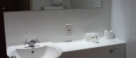 A bathroom with a white sink, mirror, and toilet. There is a towel rack above the sink and a toilet paper holder on the wall.