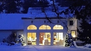 Een tweelaags huis met een sneeuw bedekte oprit en twee kerstbomen ervoor.