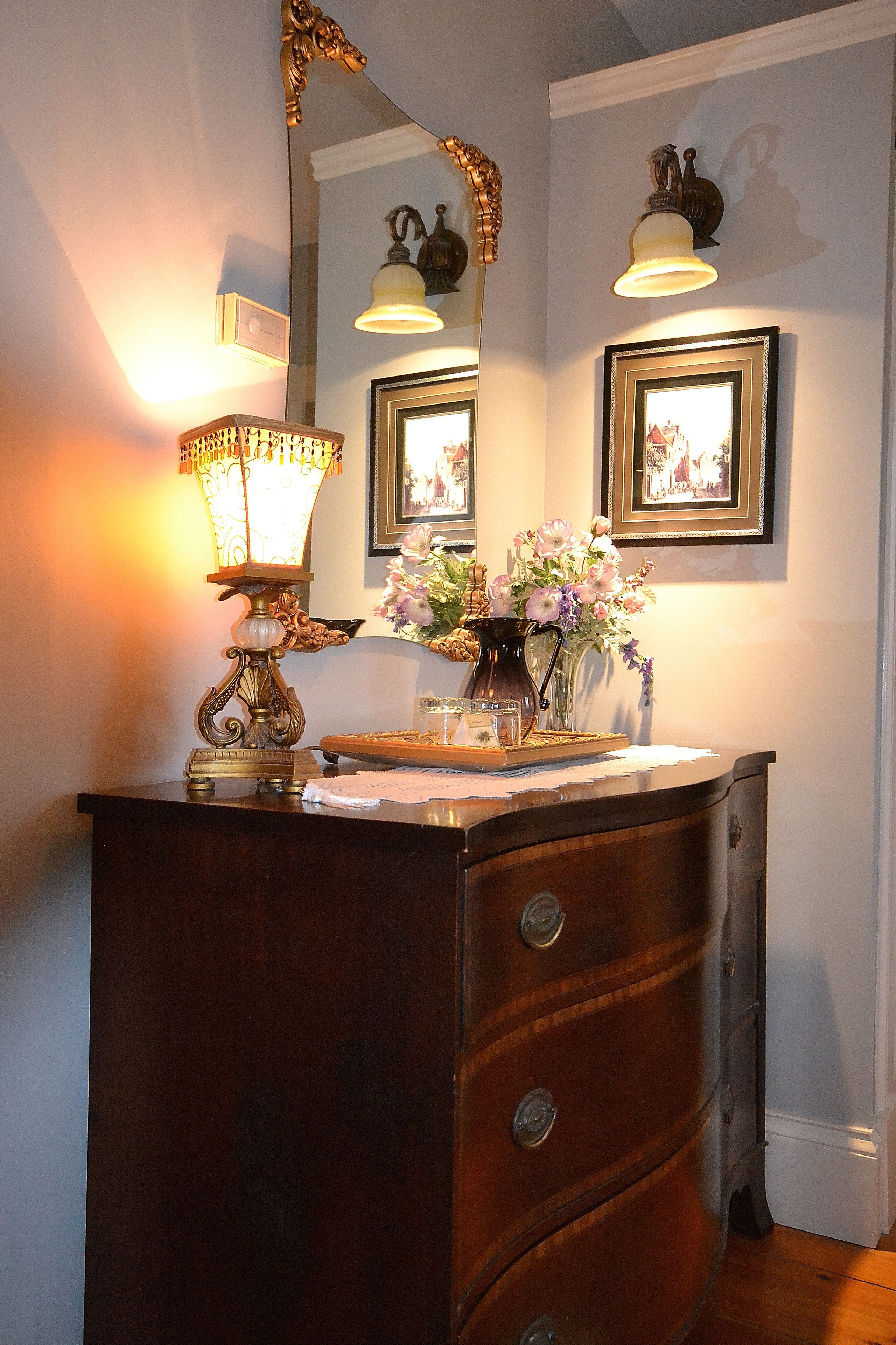 A wooden dresser with a mirror, a lamp, and a vase with flowers.