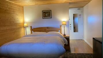 A room with a wooden ceiling and walls, a bed with two pillows, two bedside lamps, and a framed picture on the wall.