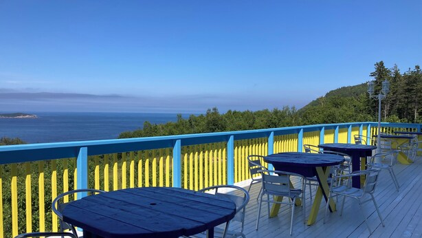 Een terras met tafels en stoelen met uitzicht op een prachtig zeegezicht.