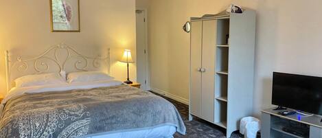 Une chambre bien rangée, avec un lit, une lampe de chevet, une armoire et un meuble pour la télévision.