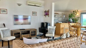Een woonkamer met een grote beige bank, een flatscreen televisie, een houten kast en een eethoek met een houten tafel en stoelen.
