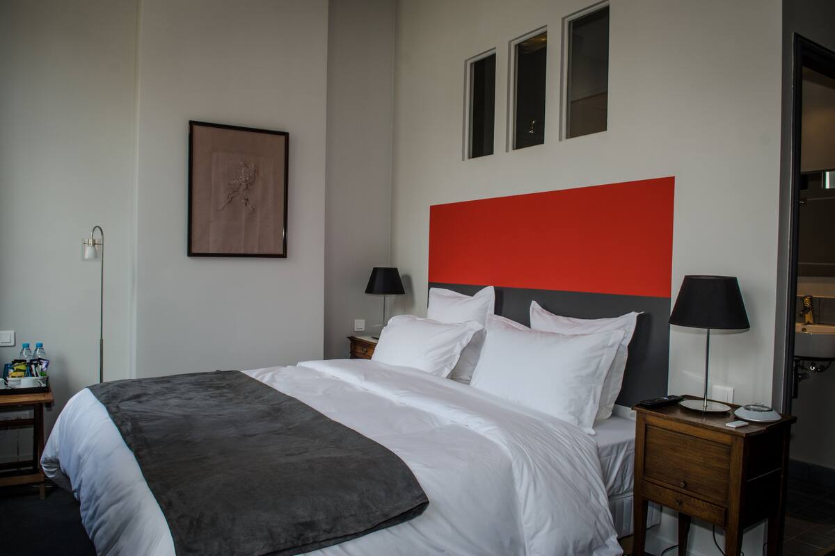 Ein Hotelzimmer mit Bett, Nachttisch, Lampe, einem gerahmten Bild und einer roten Akzentwand.