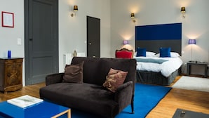 Una habitación de hotel moderna con un sofá marrón oscuro, una cama con ropa de cama azul y blanca y dos lámparas de noche.