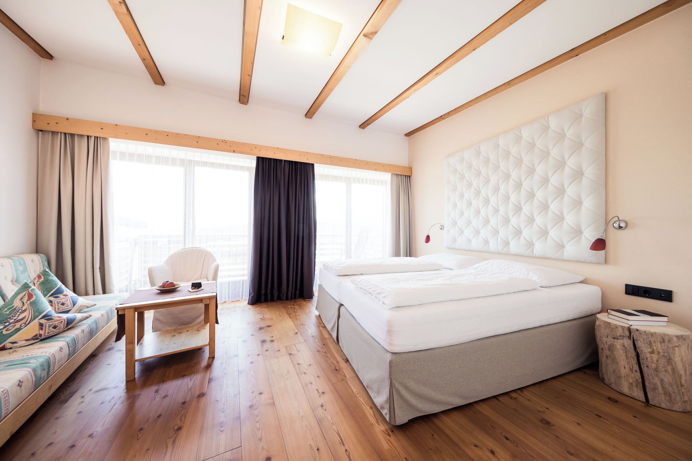 A bedroom with a bed, a sofa, a table, and a large window.